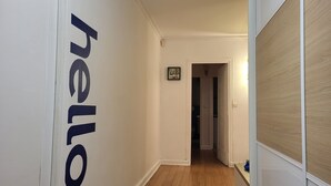 A hallway with a wooden floor, white walls, and a door with a 'hello' sign. - Superbe Appartement , Lumineux, Proche Paris (Montrouge)