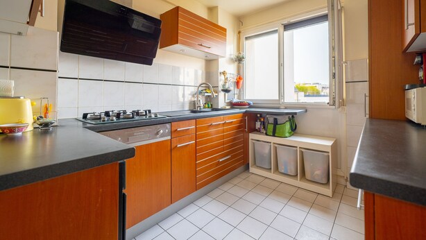 A modern kitchen with wooden cabinets, a built-in oven, and a window providing natural light. - Superbe Appartement , Lumineux, Proche Paris (Montrouge)