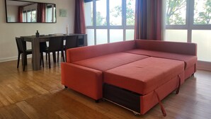 A living room with a red sofa, wooden flooring, a dining table with chairs, and large windows with curtains. - Superbe Appartement , Lumineux, Proche Paris (Montrouge)