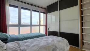A bedroom with a large window, a bed with a patterned bedspread, and a sliding closet door. - Superbe Appartement , Lumineux, Proche Paris (Montrouge)