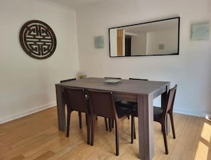 A dining area with a rectangular table, six chairs, a decorative wall piece, and a large mirror.