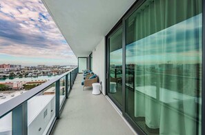 A balcony with a view of a cityscape and water, furnished with chairs and a small table.