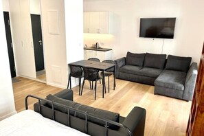 Cozy living space with a bed, sofa, and dining area, featuring a flat-screen TV and wooden flooring.
