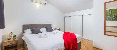 A modern bedroom with a bed, bedside tables, a nightstand, an air conditioning unit, a red throw blanket, and a large mirror.