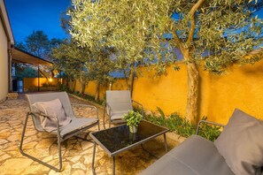 Un espacio al aire libre con una mesa, dos sillas, una planta en maceta y una pared amarilla.