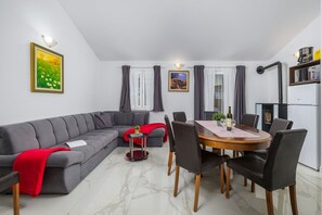 Una sala moderna con un sofá seccional gris, una mesa de comedor con sillas, una mesita auxiliar pequeña y una cocina con estufa y refrigerador.