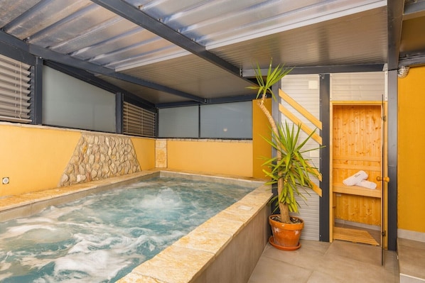 Un jacuzzi con pared de piedra, una sauna de madera y una planta en maceta.