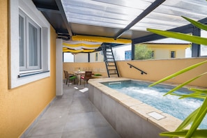 Un área de spa con un jacuzzi, una zona de estar techada y una ventana con vistas a un edificio.