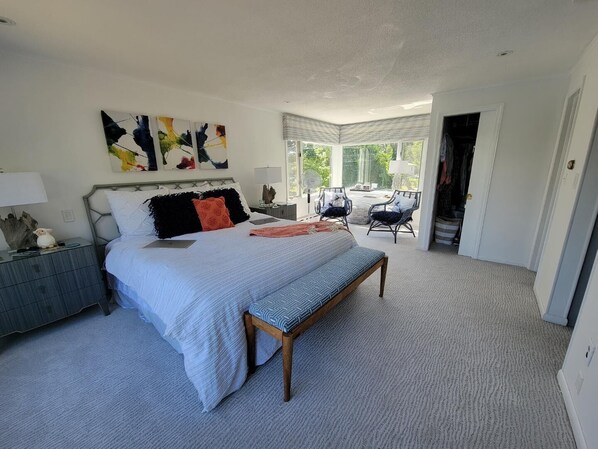 A bedroom with a large bed, a bedside table, a chair, and a view of the outdoors.