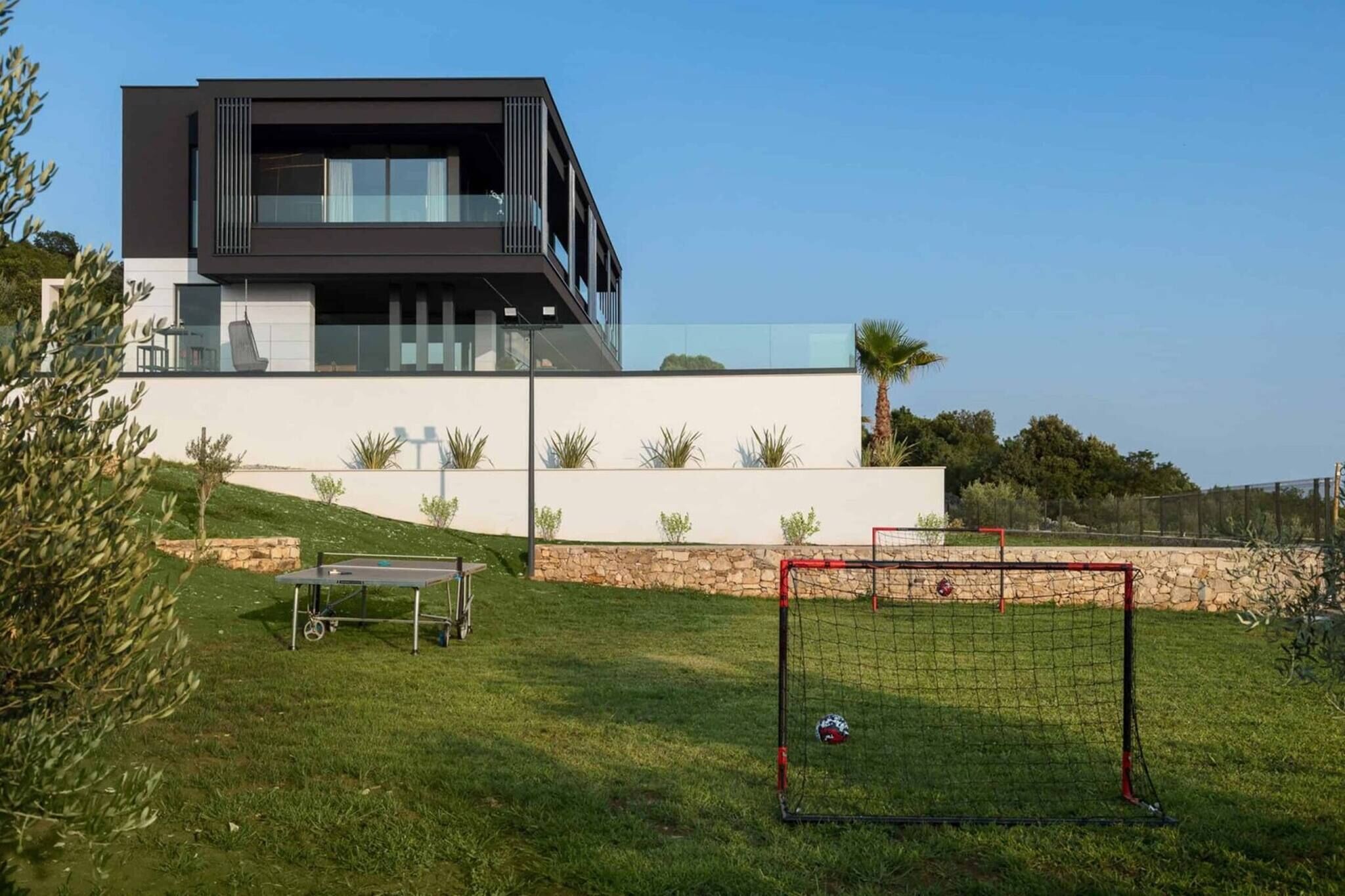 A modern two-story house with a balcony, a tennis court, and a goalpost.