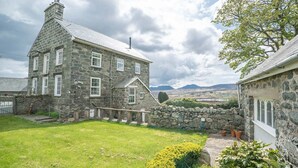 A stone house with a grassy yard and a view of mountains in the distance. - Rheithordy -  a self catering cottage that sleeps 9 guests in 5 bedrooms (Blaenau Ffestiniog)