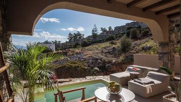 A poolside area with outdoor seating, a view of a hillside with buildings, and a clear sky.