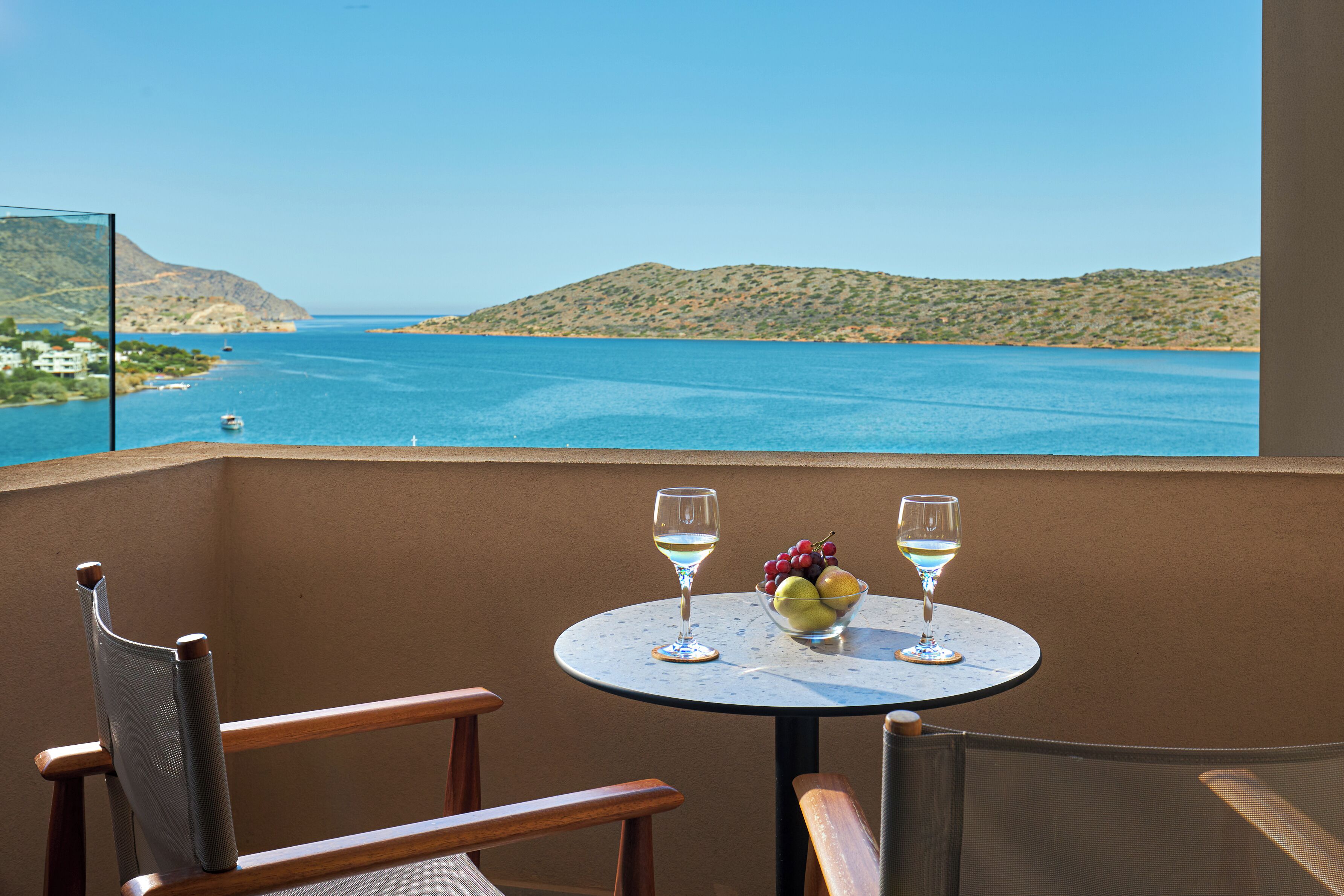 A balcony with a table, two chairs, and a view of a coastal landscape.