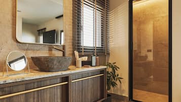 A bathroom with a large mirror, a vessel sink, a wooden vanity, a shower enclosure, and a potted plant.