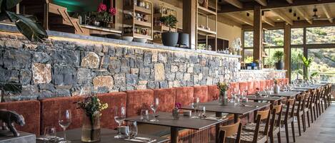 A restaurant with stone walls, wooden benches, and tables set for dining.