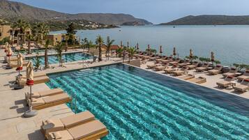 A pool area with lounge chairs and umbrellas, overlooking a calm body of water with hills in the background.