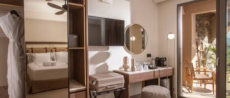 A modern hotel room with a bed, a desk with a mirror, a suitcase, and a view of the outdoors.