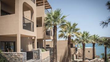 A multi-story hotel with balconies, palm trees, and a view of the sea.