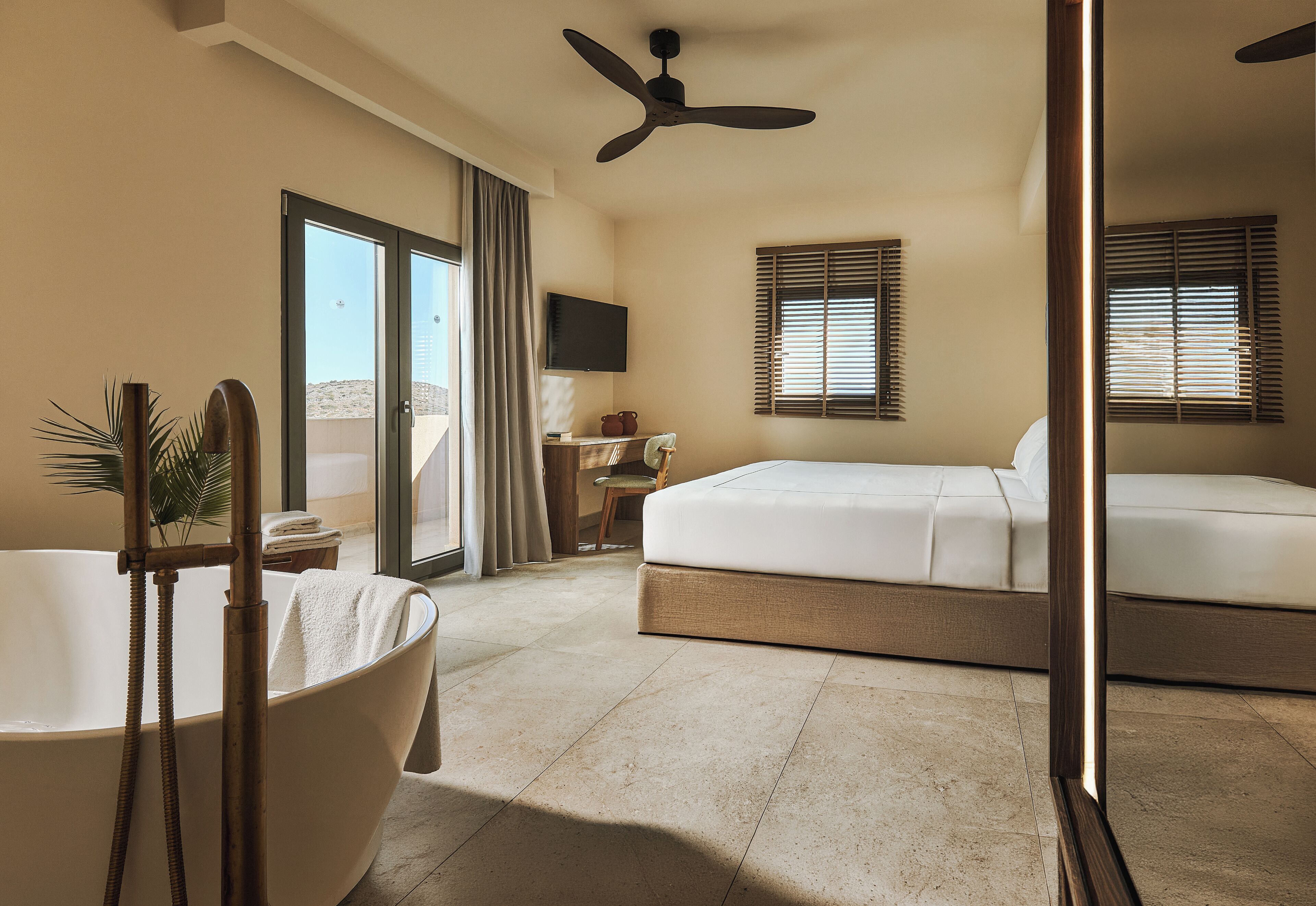 A hotel room with a bathtub, a bed, a desk with a chair, and a television on the wall.