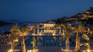 Un resort con piscina, palmeras y vista al mar de noche.