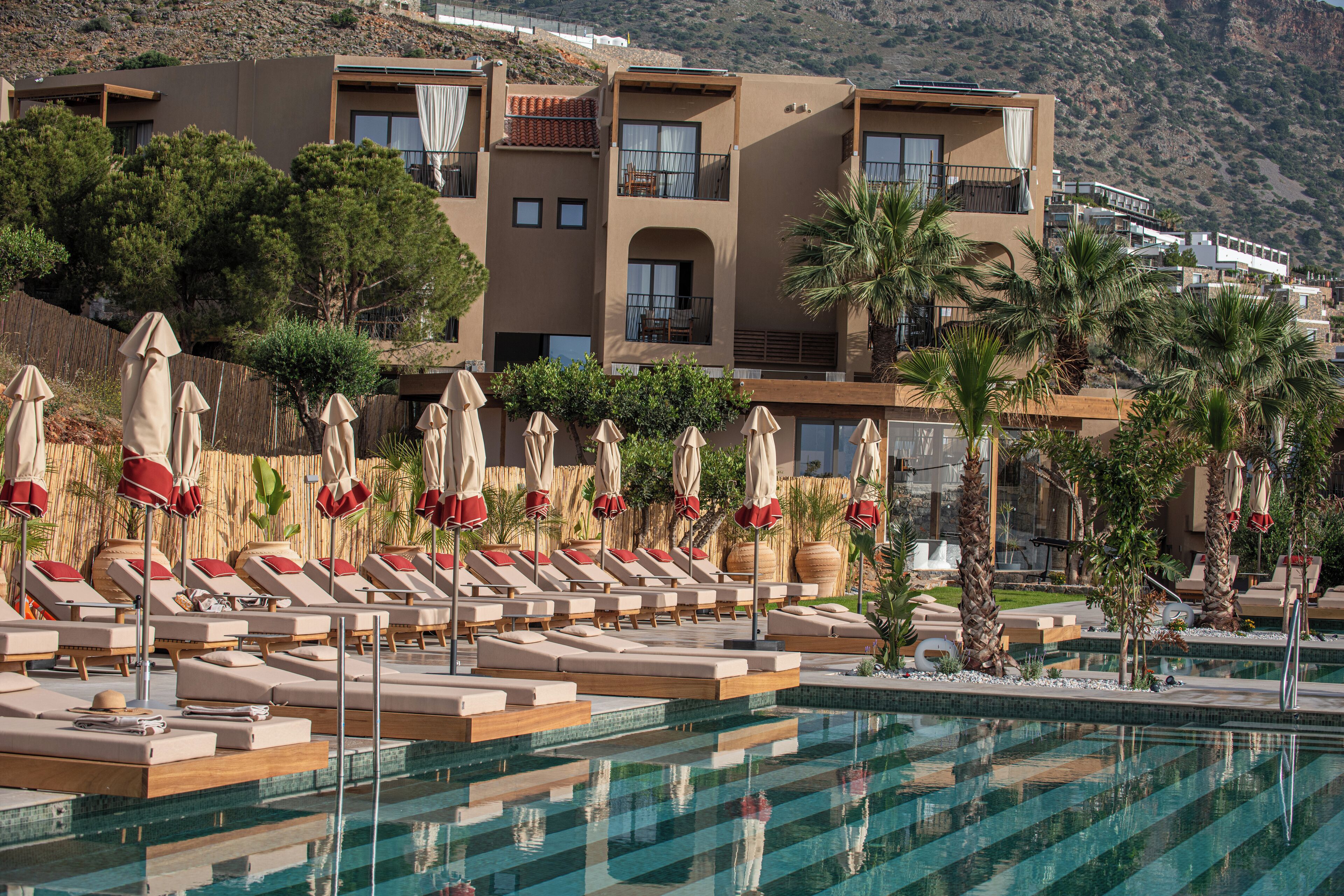 Un complexe hôtelier doté d’une piscine, de chaises longues et offrant une vue sur un paysage montagneux.