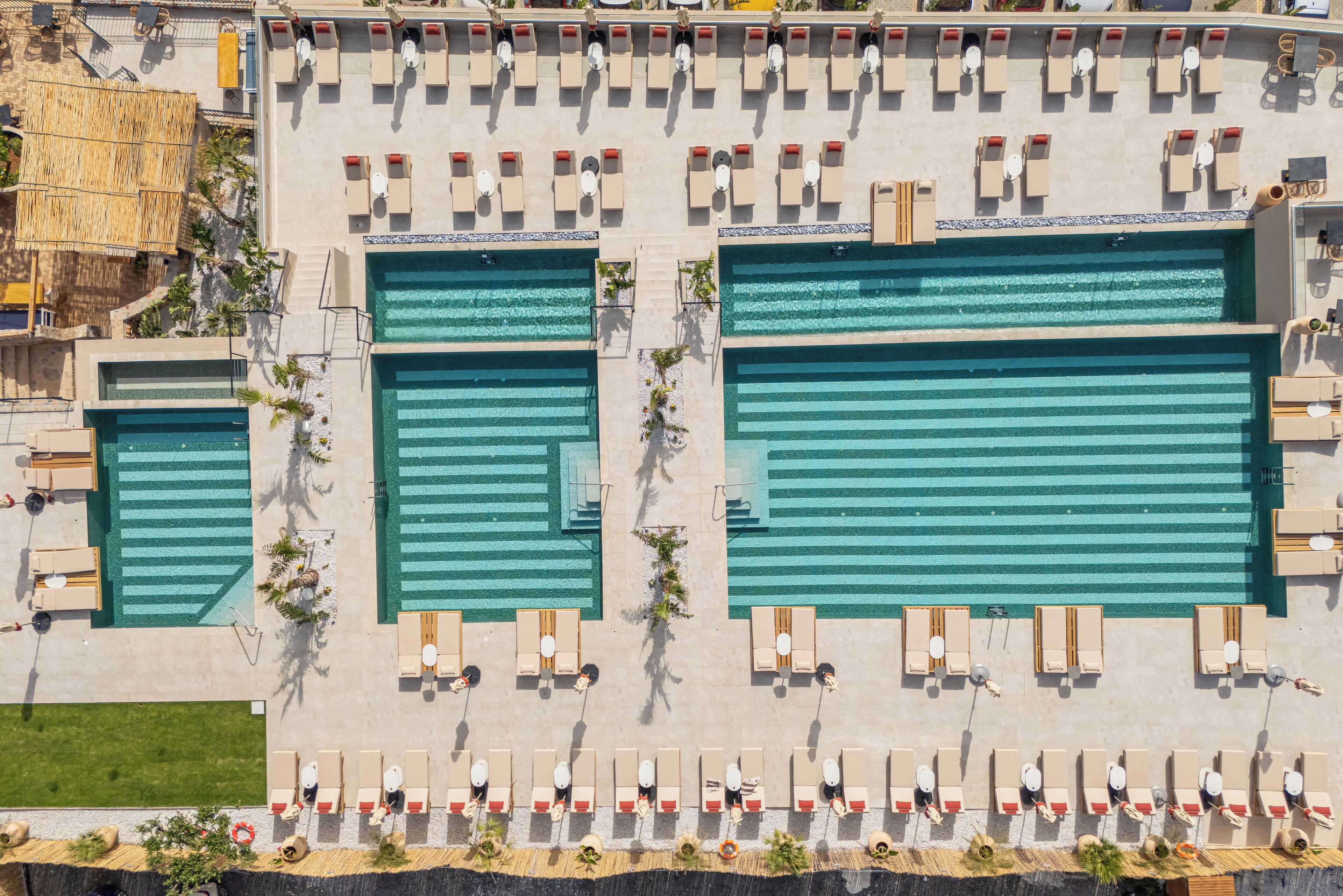 Vue aérienne d’un hôtel doté de trois grandes piscines, de chaises longues et d’une structure dont le toit est fait de chaume.