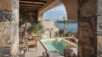 Un espacio al aire libre con paredes de piedra, una piscina, sillones de descanso y una mesa con una bebida.