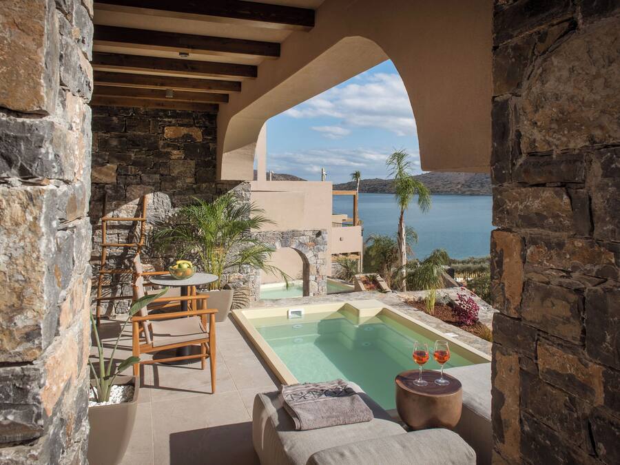 Un espacio al aire libre con paredes de piedra, una piscina, sillones de descanso y una mesa con una bebida.