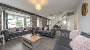 A spacious living room with grey sofas, a wooden coffee table, and a staircase leading to another level.