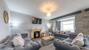 A modern living room with grey sofas, a fireplace, a stone wall, and a large window.
