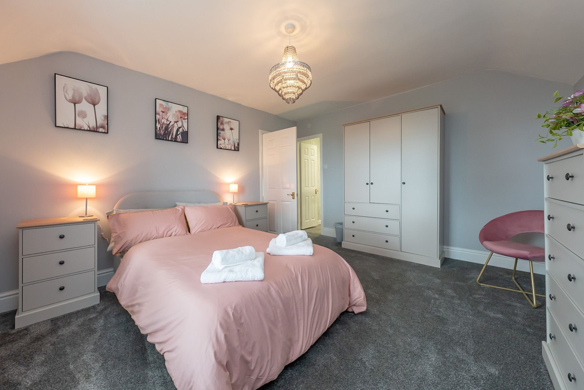 Quarto com cama, luminárias de cabeceira, guarda-roupa, cadeira e lustre.