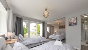 A hotel room with two beds, a sitting area with a table and chair, a chandelier, a painting, and a glass shower enclosure.