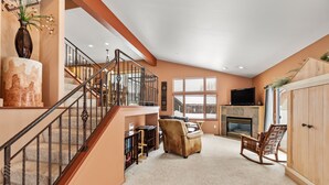 Un salon spacieux avec une cheminée, un escalier et une grande fenêtre.