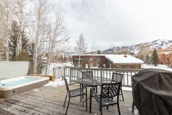 A wooden deck with a hot tub, outdoor seating, and a view of a mountain range.