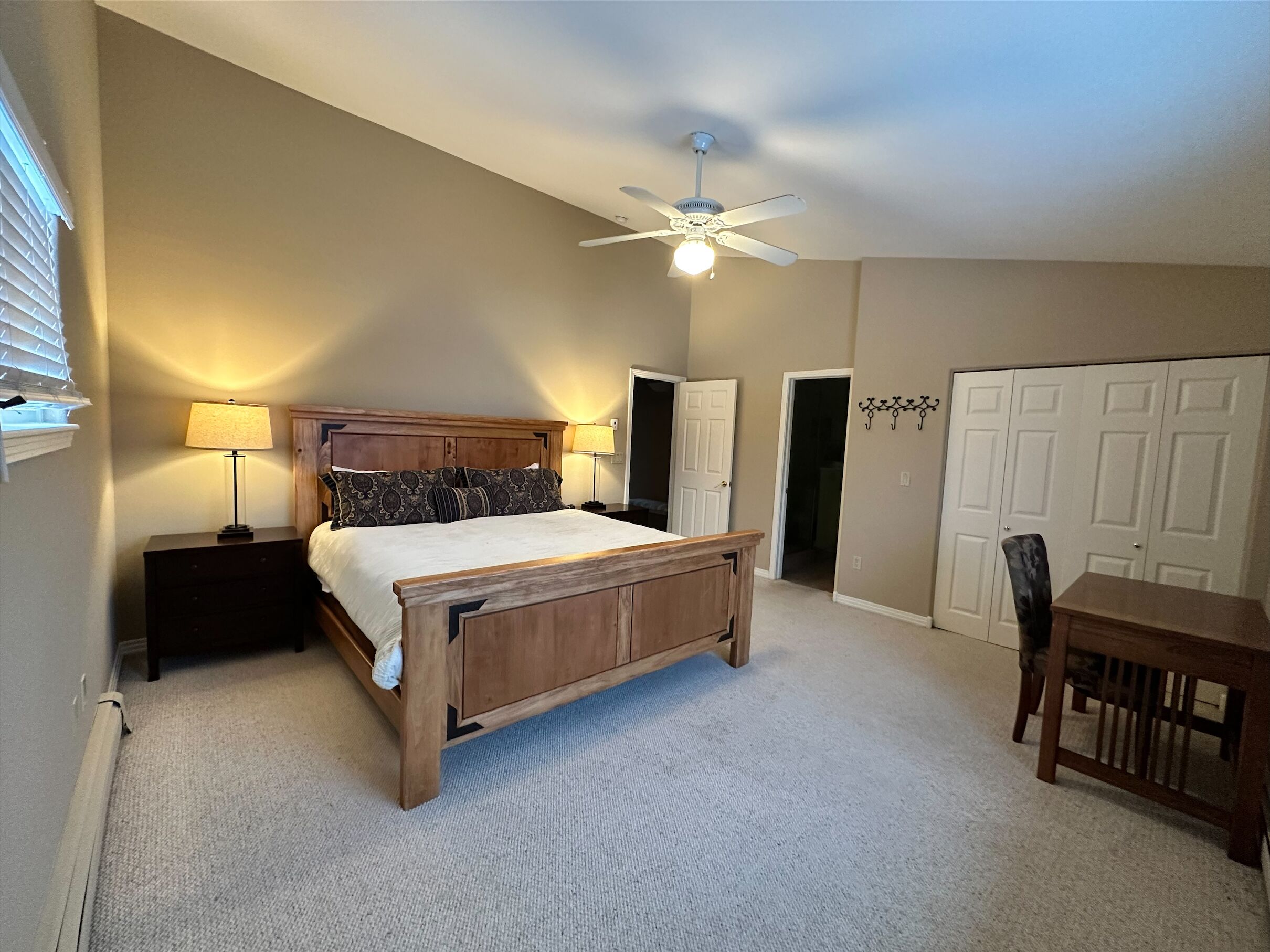 A bedroom with a wooden bed, bedside lamps, a ceiling fan, and a door leading to another room.