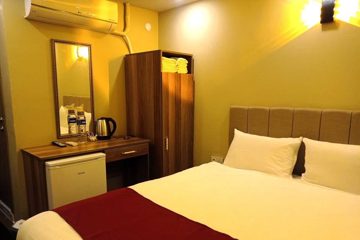 A hotel room with a bed, a bedside table, a mirror, a wardrobe, and a small refrigerator.