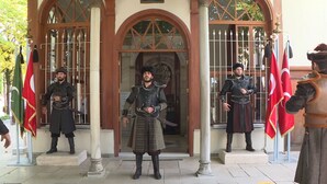 Une entrée d’immeuble avec une arche centrale, flanquée de deux gardes vêtus de costumes traditionnels.