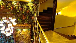 Un escalier avec une rampe, un mur décoratif orné de feuillages et des luminaires suspendus.