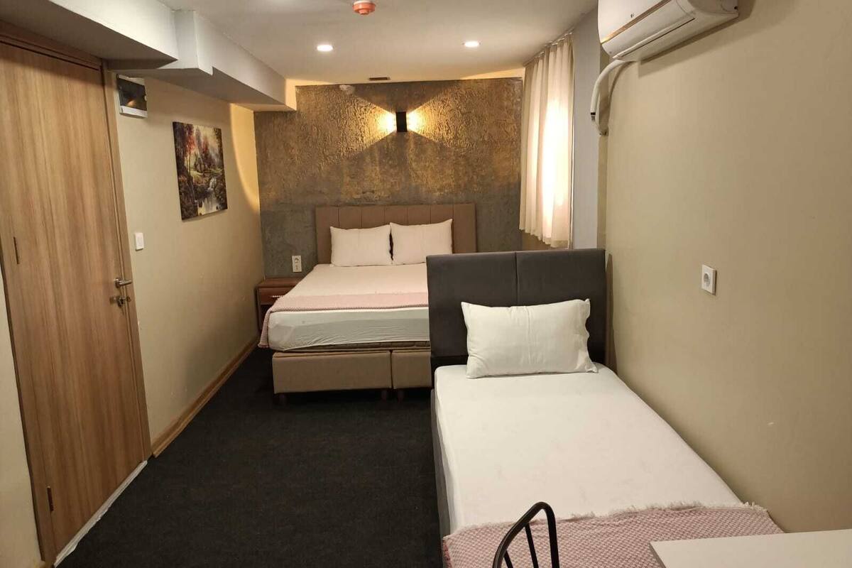 A hotel room with two beds, a wooden wardrobe, a painting on the wall, and an air conditioning unit.