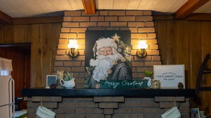 Ein Kamin mit einem weihnachtlichen Gemälde, zwei Wandleuchten und einem Schild mit der Aufschrift 'Merry Christmas'.