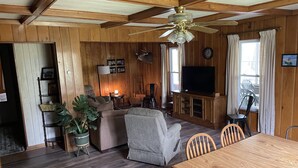 Ein Wohnzimmer mit Holzwänden, einem Deckenventilator, einem Fernseher und einem Essbereich mit Holztisch und Stühlen.