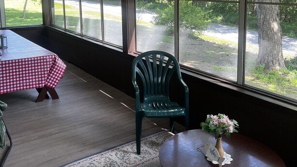 Ein Zimmer mit Tisch und Stühlen, großen Fenstern mit Blick auf Bäume und eine Straße sowie Holzboden.