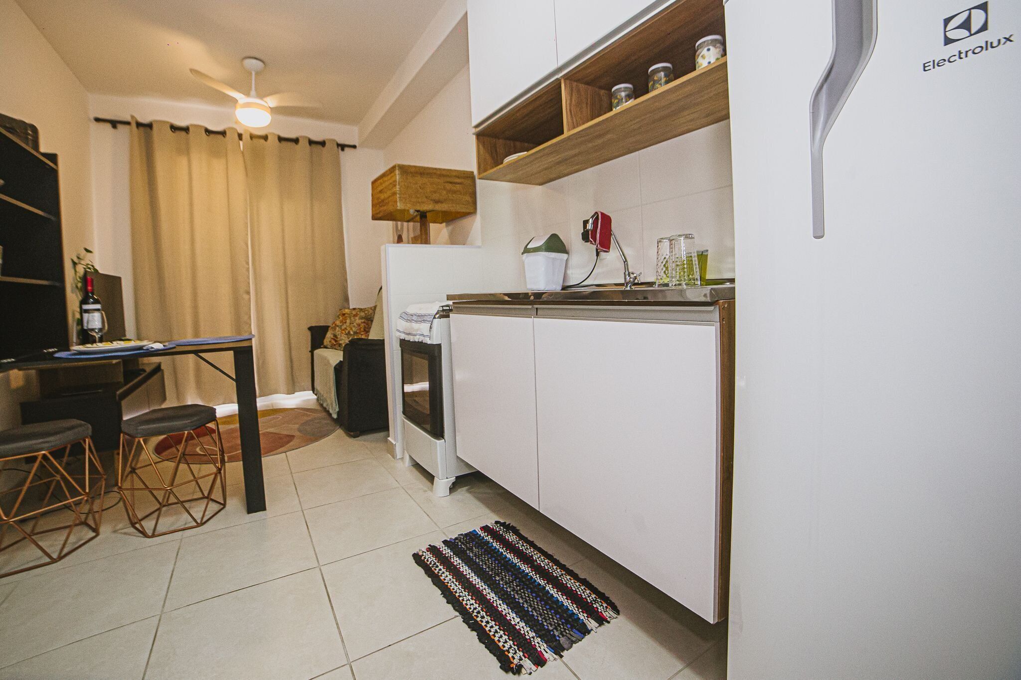 A compact kitchen with white cabinets, a wooden countertop, a ceiling fan, and a small dining area with stools.