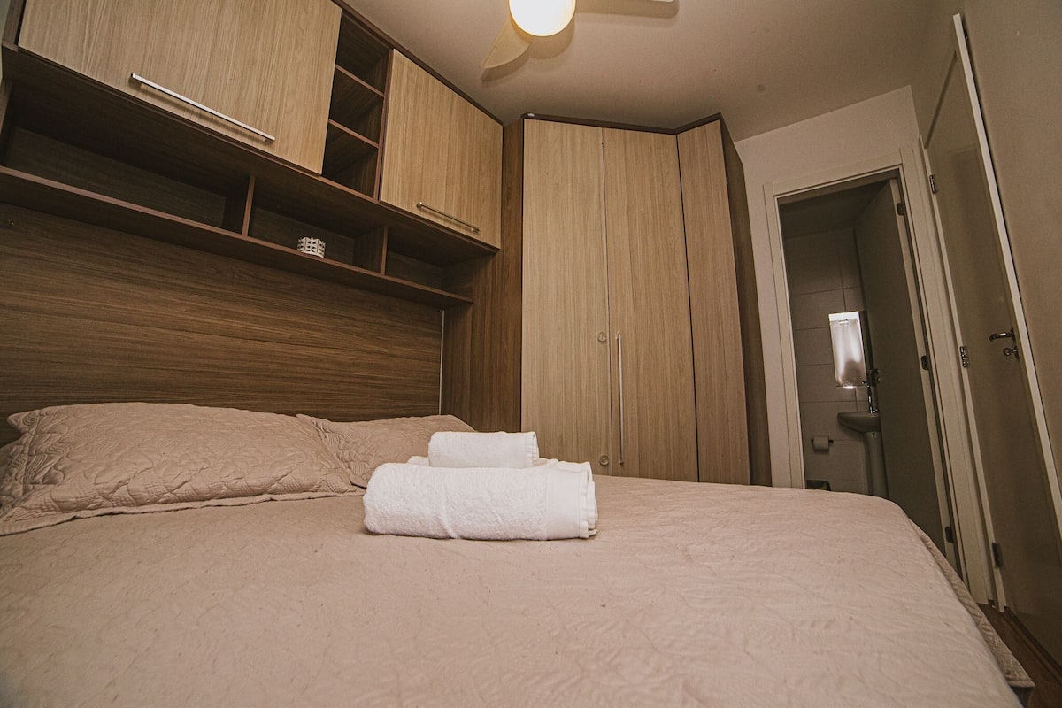 A neatly made bed with a headboard, a wooden wardrobe, and a bathroom door.