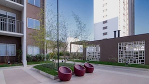 A modern outdoor area with a paved walkway, three red planters, and a building with balconies and windows. - Chácara Santo Antonio - Laguna 430 (São Paulo)