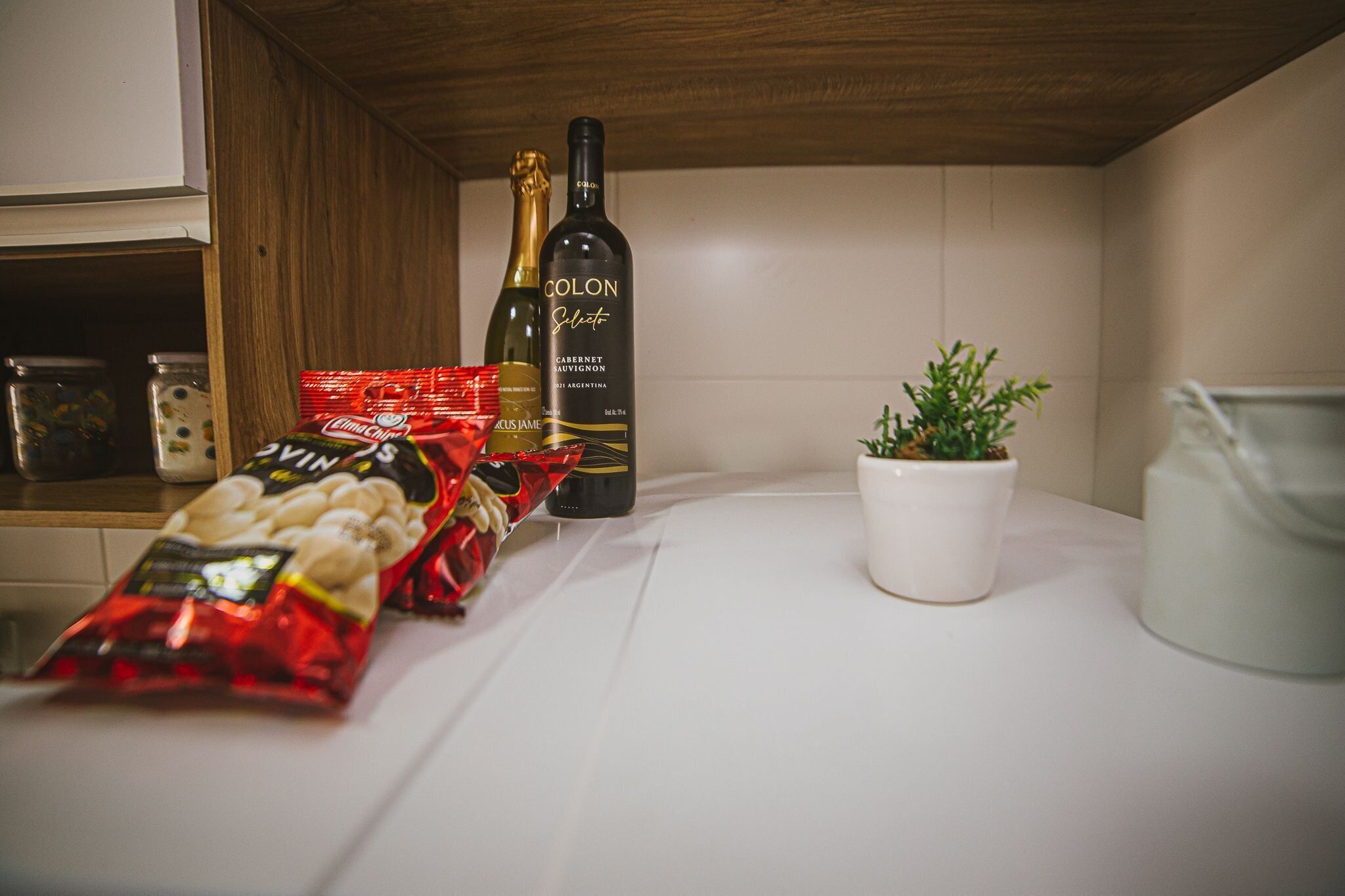 A kitchen counter with a bottle of wine, a potted plant, and a bag of snacks.