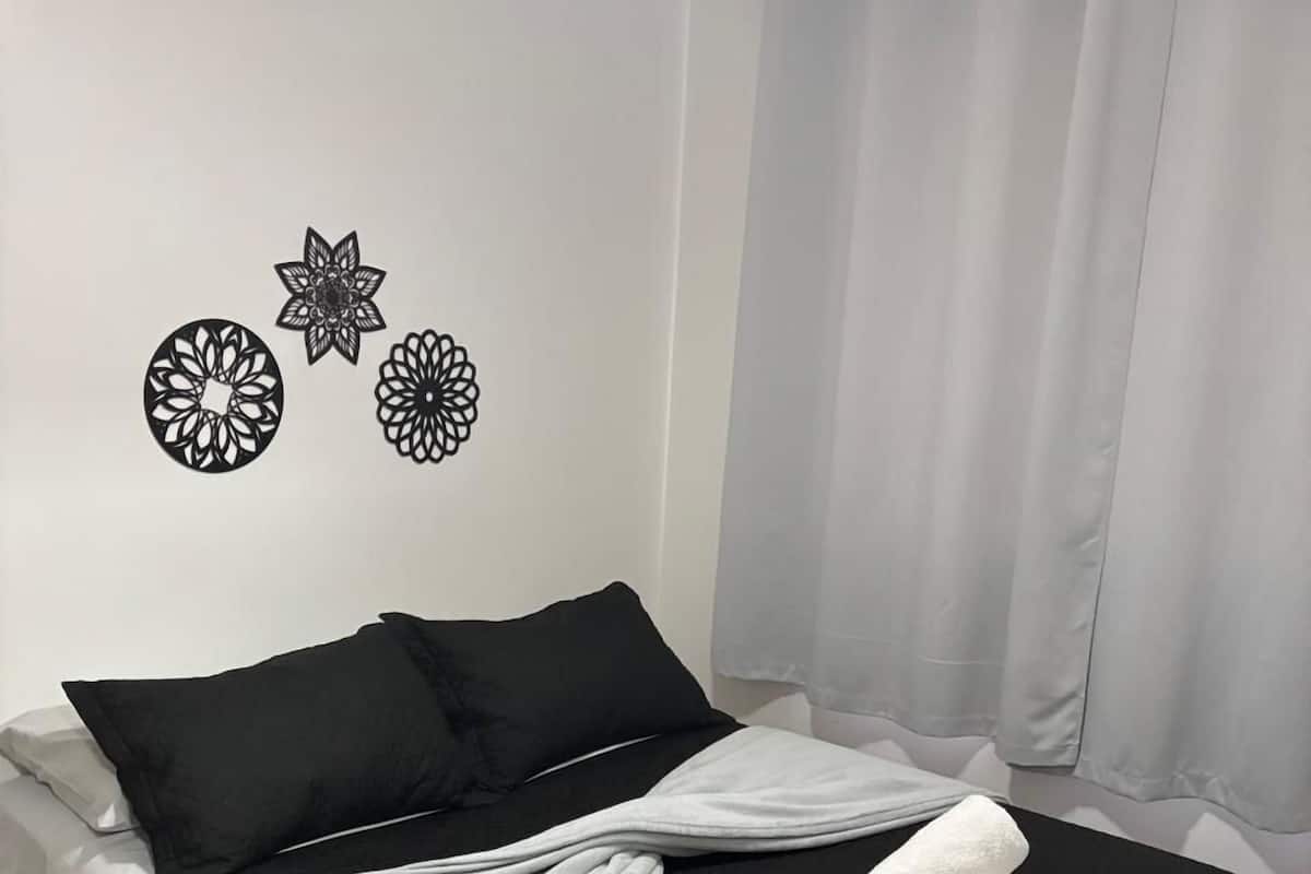 A neatly made bed with black and white bedding, a grey blanket, and two rolled towels.