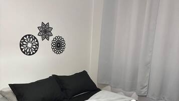 Un letto rifatto con biancheria a contrasto bianco e nero, una coperta grigia e due asciugamani arrotolati.