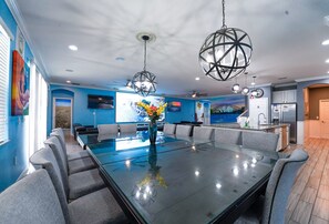 Una cocina moderna con una isla central, un comedor con mesa de vidrio y una sala de estar con televisor grande.