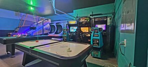 Una mesa de billar rodeada de máquinas recreativas, incluyendo una con temática de 'Fast and Furious'.